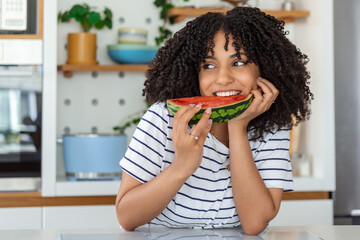 Pretty young girl holding slice of watermelon in front of her face.
