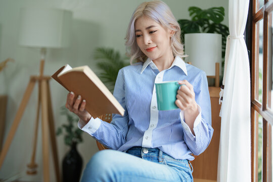 Portrait of an Asian business woman drinking coffee while reading book with a computer on her desk