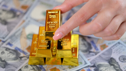 Woman hand holding bank golden ingots, cash on background