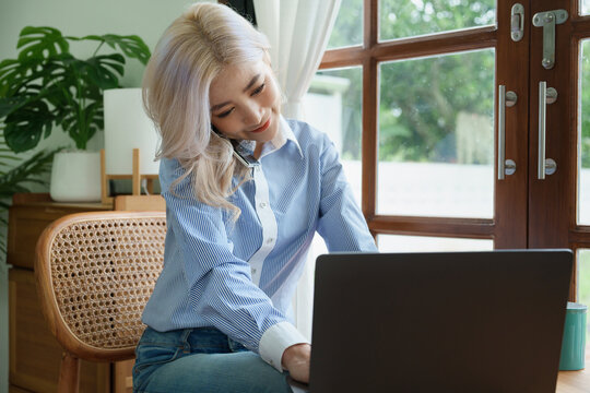 Portrait of a beautiful Asian teenage girl using her phone and computer sitting on the sofa at home