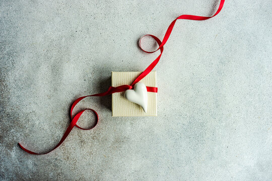 Overhead view of a white gift box tied with a red ribbon and decorated with a ceramic heart ornament