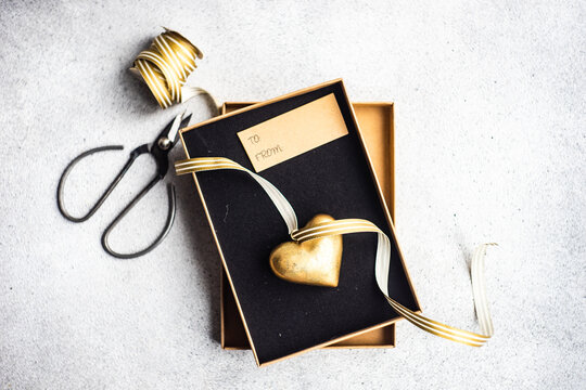 Overhead view of an open gift box with a gold hear ornament and a gift tag