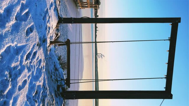 An empty wooden swing moving outdoors, without people. Beautiful view of the pond covered with snow and ice against the background of the smoking pipes of the Topol-M rocket factory. Russia