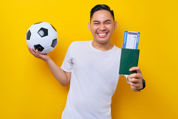excited young Asian man football fan wearing a white t-shirt holding a soccer ball and passport...