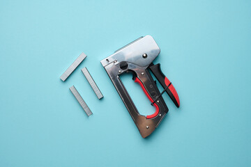 Household manual stapler and staples on a blue background, top view