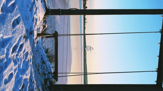 An empty wooden swing moving outdoors, without people. Beautiful view of the pond covered with snow and ice against the background of the smoking pipes of the Topol-M rocket factory. Russia