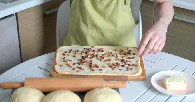 Cruffin easter pastry cooking at home concept. Unrecognizable caucasian person sprinkles raisins on kneaded dough smeared with butter. High quality 4k video footage
