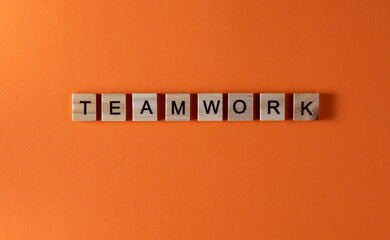 Teamwork word phrase in wooden letters. Motivation and slogan. Orange background.