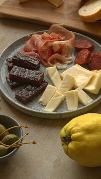 Plate and bowls with tapas: cheese, chorizo sausage, ham, membrillo sweet paste, olives, capers, confit tomatoes. Table spin. Vertical video.