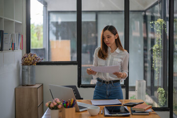 Asian businesswoman standing and holding documents while working in an office