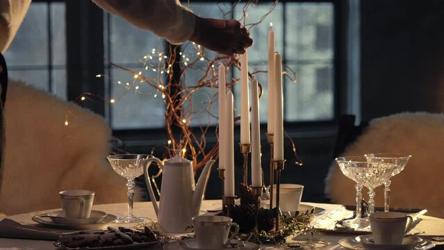 Woman hand light paraffin candles using match. Christmas table setting.