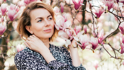 Obraz na płótnie Canvas A closeup portrait of an attractive woman by a blooming magnolia tree. In bloom. Spring concept.