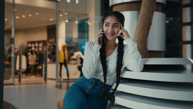 Young businesswoman student ethnic iranian arabian 20s woman girl shopper speak phone sit in shopping mall use wireless mobile connection calling friend talk gossip by telephone distant communication