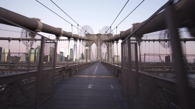 POV view. Driving by bicycle along the Brooklyn bridge, a hybrid cable-stayed and suspension bridge in NYC approaching the main tower. Morning. Skyscrapers on the background