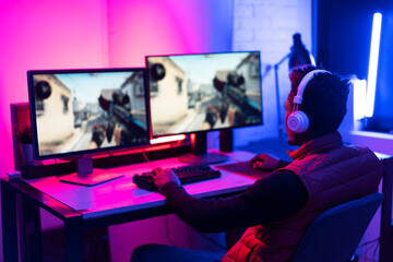 Young African man playing video game on computer. Streamer guy sitting at home and plays another match