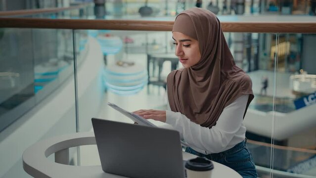 Arabian turkish muslim woman student islamic businesswoman freelancer in hijab work distant on laptop check commercial documentation paper documents enter electronic data pay bills online e-business