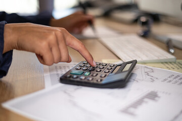 Close up Woman hand types on a calculator. Desk with keyboard and financial reports. Office administrator  calculates financial figures. Accounting, ordering and back office services.