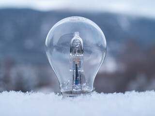 Close-up of a light bulb sticking up from soft snow with a blurred winter landscape in the background