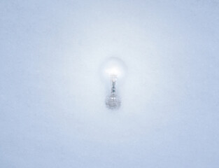 Shining Light bulb laying in the white snow while illuminating its surroundings.