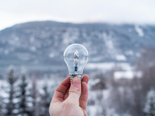 Hand holding a lightbulb up in front of a snowy mountain landscape