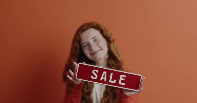 Ginger woman advertising sale. Portrait of happy woman standing with sale card