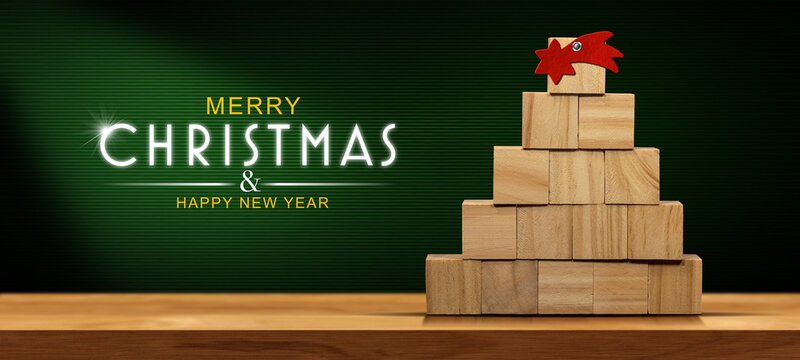 Small wooden Christmas tree (made of small wooden cubes) with a red comet star on a wooden table with copy space and text Merry Christmas and Happy New Year. 
