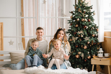 Mom, dad hug daughter and son on the bed near Christmas tree. Happy New Year and Merry Christmas. Christmas decorated interior in home. The concept of family holiday. Close up. Winter decor.