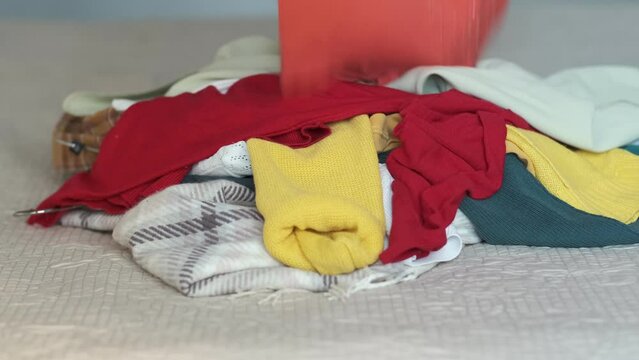 woman throws unnecessary clothes on the bed. an unrecognizable person rakes up a pile of clothes with his hands and takes them away. the concept of textile recycling, excess consumption