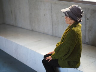 屋内のベンチで座る高齢日本人女性の横顔