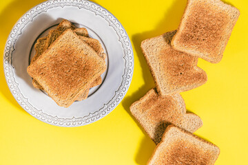 Tower of toasted bread slices on gray plate and several slices of toasted bread on yellow background
