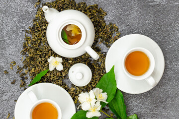 jasmine flower tea in cups and teapot, herbal drink, dried jasmine leaves and beautiful flowers, top view, dark background, medicinal, herbal tea, dietary