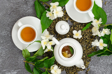 jasmine flower tea in cups and teapot, herbal drink, dried jasmine leaves and beautiful flowers, top view, dark background, medicinal, herbal tea, dietary