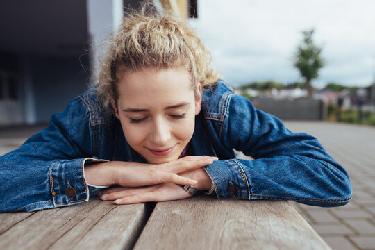 Young smiling blonde girl lying on wooden bench with her eyes closed