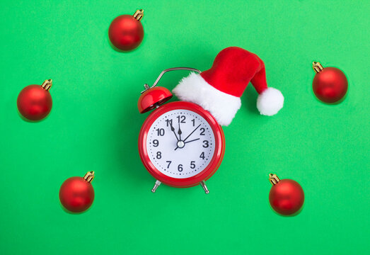 Red alarm clock with Christmas Santa hat and red bead on the green background. Close-up. Copy space.