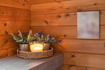 Burning candle in glass candlestick with plants as a decor in a bathroom with wooden walls and blurred picture