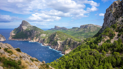 Landscape shot of the wild coastal landscape of Cap Formentor in Mallorca Spain. Cliffs in the sea on a sunny day with blue sky and clouds. Green landscape with a lot of forest from above.