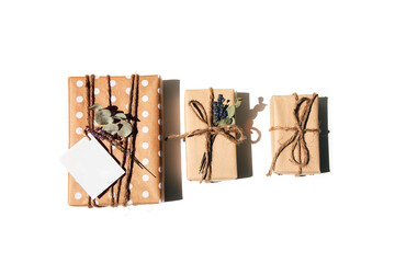 Fototapeta na wymiar A set of handmade gifts in kraft paper, tied with wide twine, decorated with dry flowers on a white table. Top view