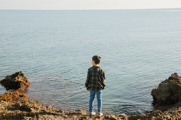 Fototapeta na wymiar boy by the sea. Child goes on vacation by the sea. Child alone by the water. Dangers on a beach holiday