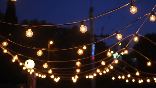 A view from below of a lot of small light bulbs, a festive garland illuminating the night sky.