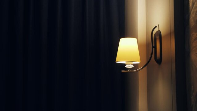 Person turn on wall lamp in room hotel.