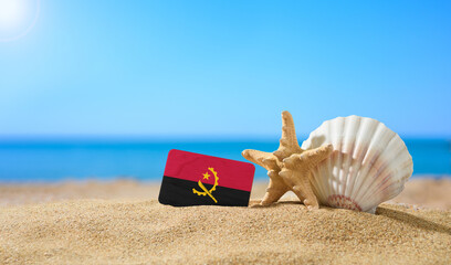 Fototapeta na wymiar Tropical beach with seashells and Angola flag. The concept of a paradise vacation on the beaches of Angola.
