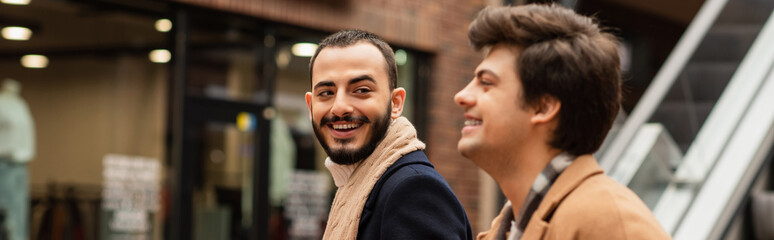 happy bearded gay man looking at blurred boyfriend on urban street, banner.