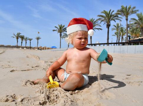 Portrait of a cute toddler boy wearing Santa hat playing on the beach. Christmas vacation with kids concept