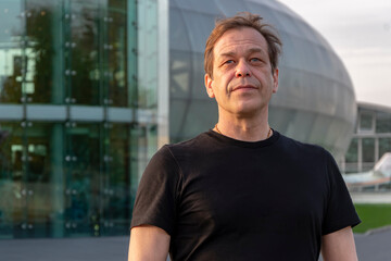 Street portrait of a man 40-50 years old in a black T-shirt on a blurred background of a glass...