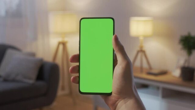 Handheld Camera: Point of View of Young Man at Home Living Room Holding Chroma Key Green Screen Smartphone Watching Content With Touching or Swiping Up and Tap Center.