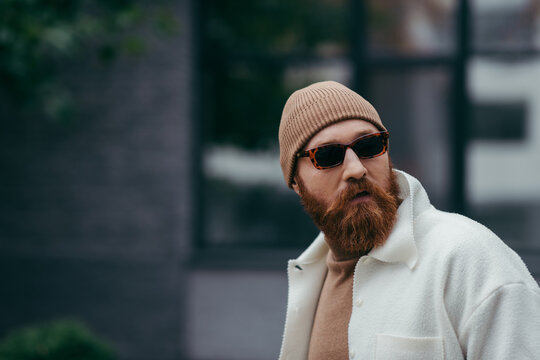 bearded hipster in stylish sunglasses and white shirt jacket looking away.