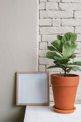 Blank white empty picture frame mockup, plant in pot on window sill on sunny day. Office interior. Copy space. Artwork showcase.