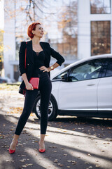 Business woman with notebook standing by electric car charging