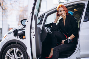 Business woman sitting in electric car at the electric charging station