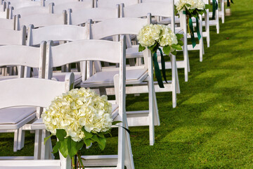 White chairs with flowers on an outdoor wedding day